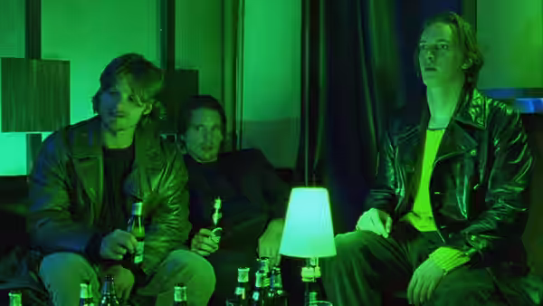 three young men sitting on a couch surrounded by empty bottles under green light