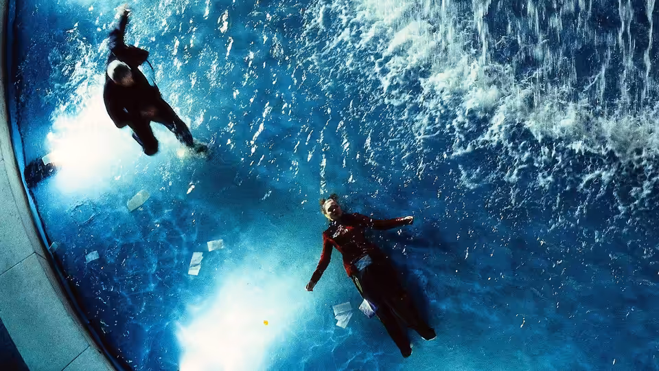 a man and a woman floating underwater amid scattered papers and bright lights