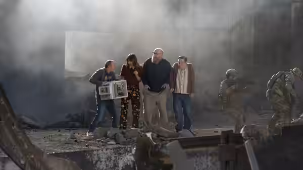 Group standing amid rubble and smoke as armed soldiers approach from the side