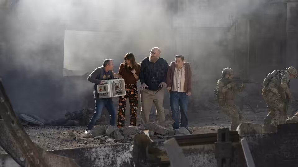 Group standing amid rubble and smoke as armed soldiers approach from the side