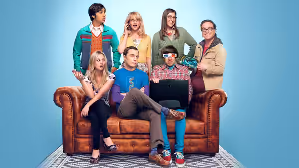 Penny, Leonard and Sheldon sit on the couch as friends stand behind them