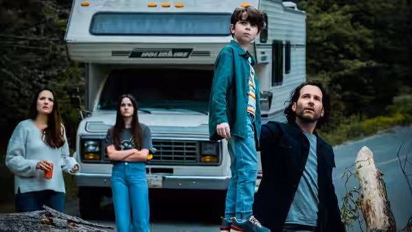 A family standing in front of an RV on a forest road