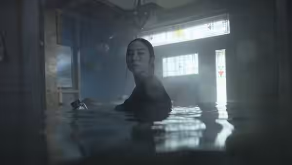 Woman stands chest deep in water inside flooded room with floating debris