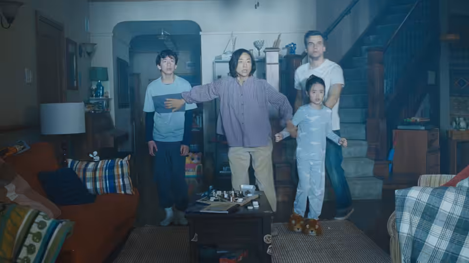 Woman in purple sweater gestures widely in living room with boy man and girl