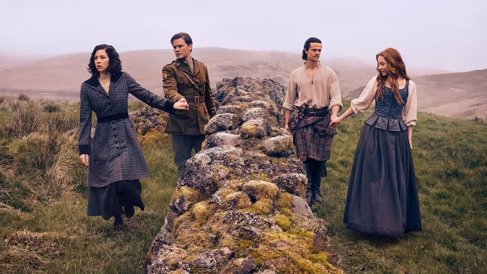 Four people holding hands across a mossy stone wall in the hills