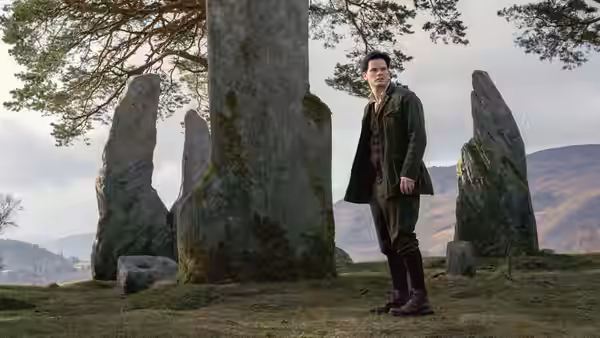 Man standing among ancient standing stones in a grassy field