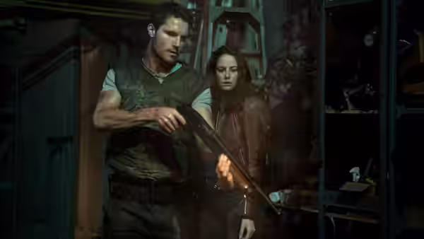 Chris Redfield (Robbie Amell) holds a shotgun beside Claire Redfield (Kaya Scodelario) in a dim room