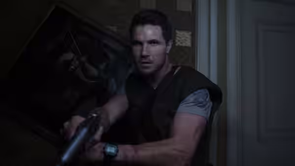 Chris Redfield (Robbie Amell) grips a pistol while crouching in a dark room