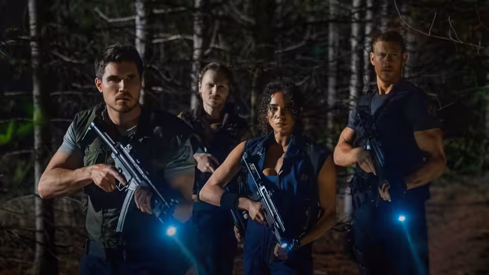 Chris Redfield (Robbie Amell) and Jill Valentine (Hannah John-Kamen) stand armed in a dark forest
