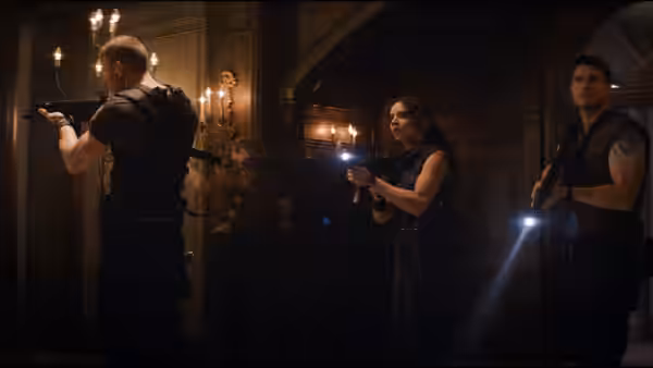 Albert Wesker (Tom Hopper) aims a shotgun in a candlelit hallway as two others watch