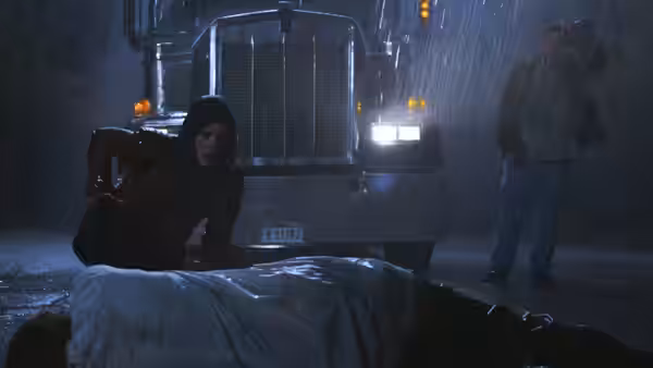 Claire Redfield (Kaya Scodelario) kneels by a body on a rainy road near a truck