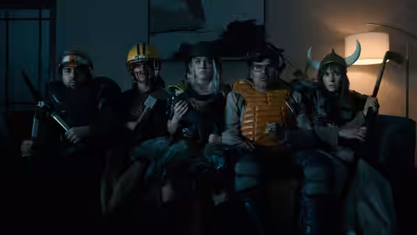 Five people in helmets and armor sit armed on a living room couch