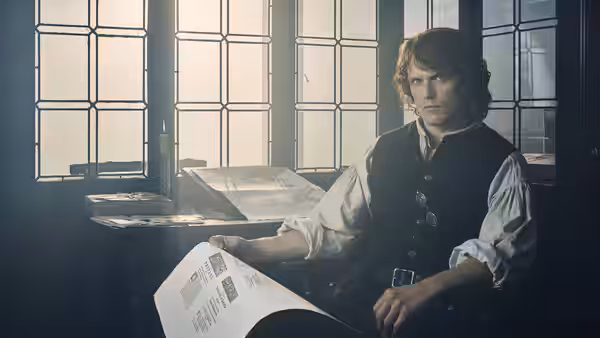 Jamie Fraser (Sam Heughan) reading a document by a window in a study