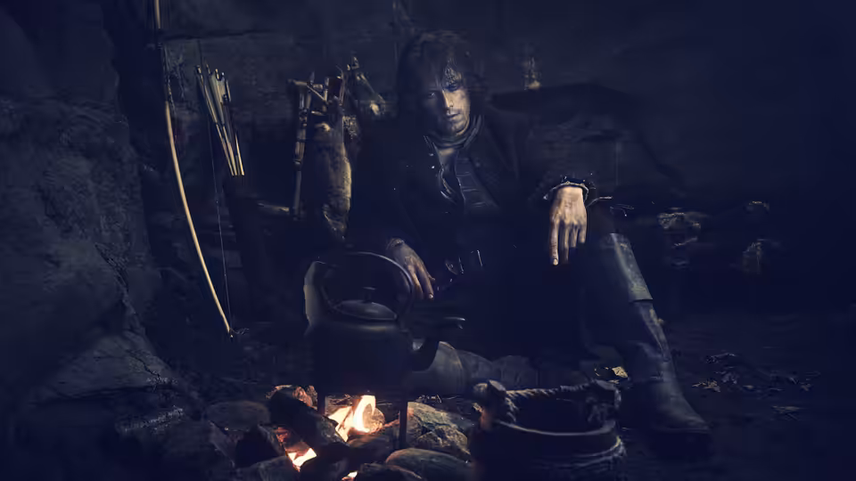Jamie Fraser (Sam Heughan) tending a kettle over a fire in a cave
