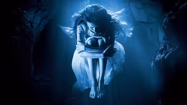 A woman curls underwater in a blue-lit rocky passage