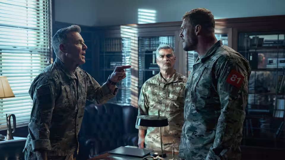 81 (Alan Ritchson) facing a pointing officer during an argument in an office
