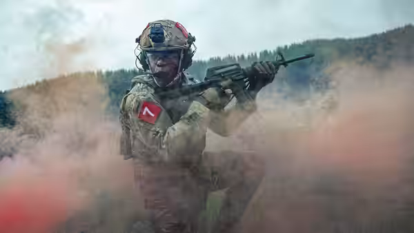 Soldier kneeling and aiming a rifle through red smoke in a forest