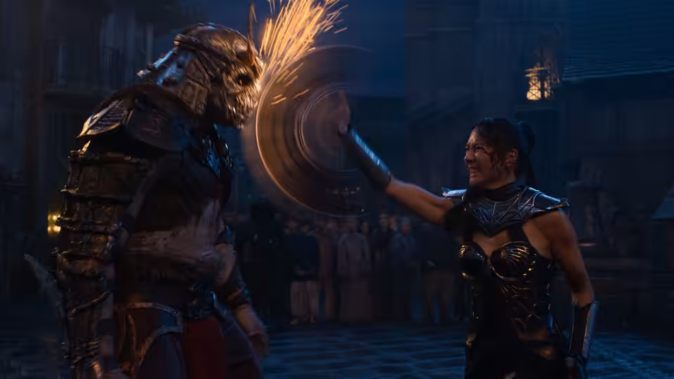 Kitana (Adeline Rudolph) wielding a spinning blade against an armored foe in a stone arena