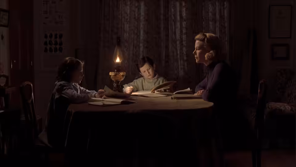 Grace Stewart (Nicole Kidman) and her children read by lamplight at the table