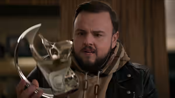 A bearded man holding a large silver award trophy