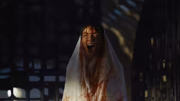 A bloodied woman in a white veil screams inside a shadowy chamber