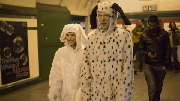 A couple in rabbit and dalmatian costumes walk through a subway station