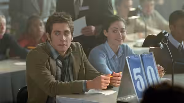 Sam Hall (Jake Gyllenhaal) and Laura at a desk holding a quiz card marked 50