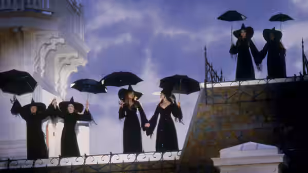Women in black dresses and hats holding umbrellas on a balcony