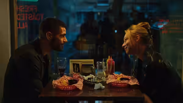 a man and woman face each other across a diner table laden with burgers and drinks