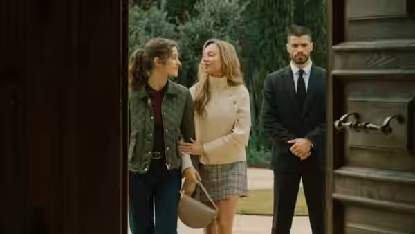 two women stand close together at an open doorway while a suited man watches nearby