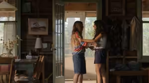 Two young women stand close together inside a rustic cabin