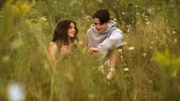 A young woman and man sit together in a meadow of wildflowers