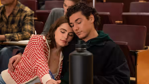 Students rest their heads together while seated in a lecture hall