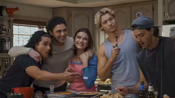 Four friends pose together around a kitchen counter with pizza