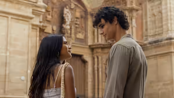 Oriah (Maia Reficco) and Julián (Fernando Lindez) standing close outside a stone building