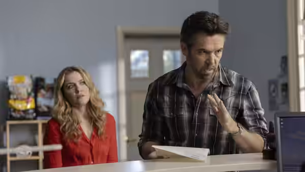 Gordon (Patrick Brammall) reading papers while Ashley (Harriet Dyer) stands behind him