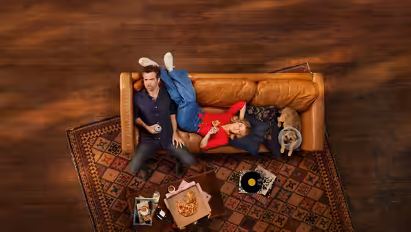 Ashley (Harriet Dyer) and Gordon (Patrick Brammall) lounging on a leather couch with their dog