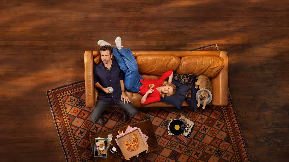 Ashley (Harriet Dyer) and Gordon (Patrick Brammall) lounging on a leather couch with their dog