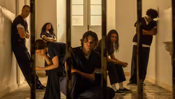 young adults in blue jumpsuits inside a prison behind metal bars