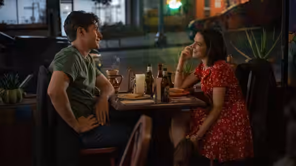 A man and a woman sit at a table with pizza and beer bottles in a diner