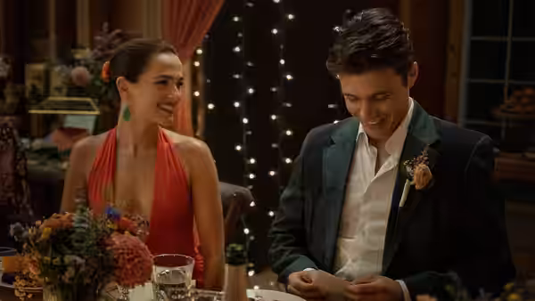 A woman in a red dress smiles at a man in a suit reading a card at dinner