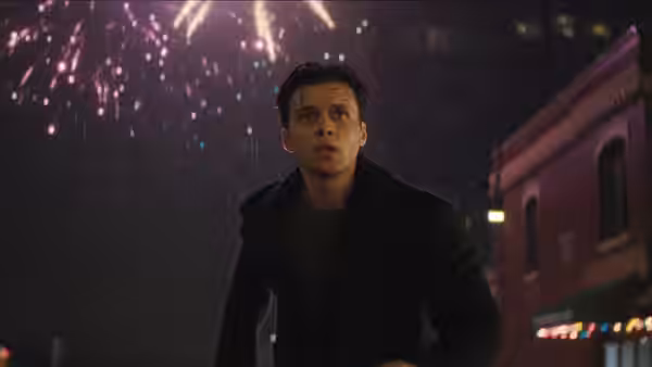 A man stands in the rain at night looking up at fireworks in the sky