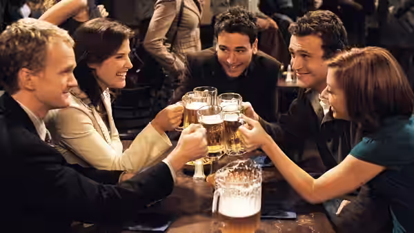 Barney, Robin, Ted, Marshall and Lily raising glasses of beer in a toast