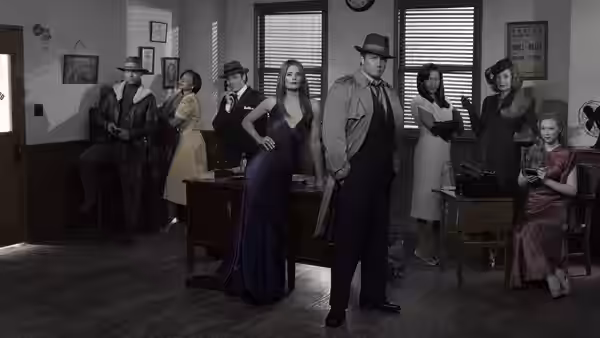 A group of people in vintage attire posing inside an old-fashioned office with desks