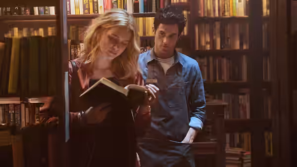Joe Goldberg (Penn Badgley) watching a woman reading in a library