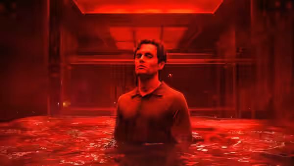 Joe Goldberg (Penn Badgley) standing chest-deep in red liquid