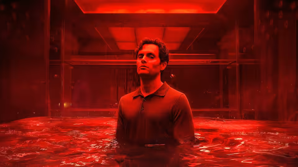 Joe Goldberg (Penn Badgley) standing chest-deep in red liquid