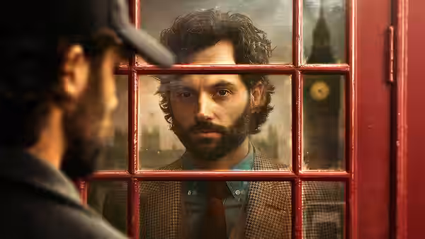 Joe Goldberg (Penn Badgley) peering through a red window pane