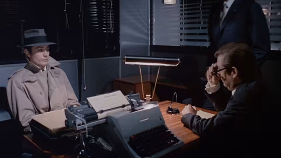 Jef Costello (Alain Delon) sits across a desk from an official in an office