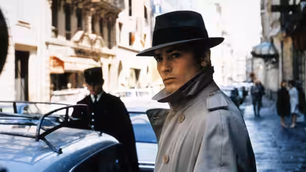 Jef Costello (Alain Delon) stands beside a car on a Paris street